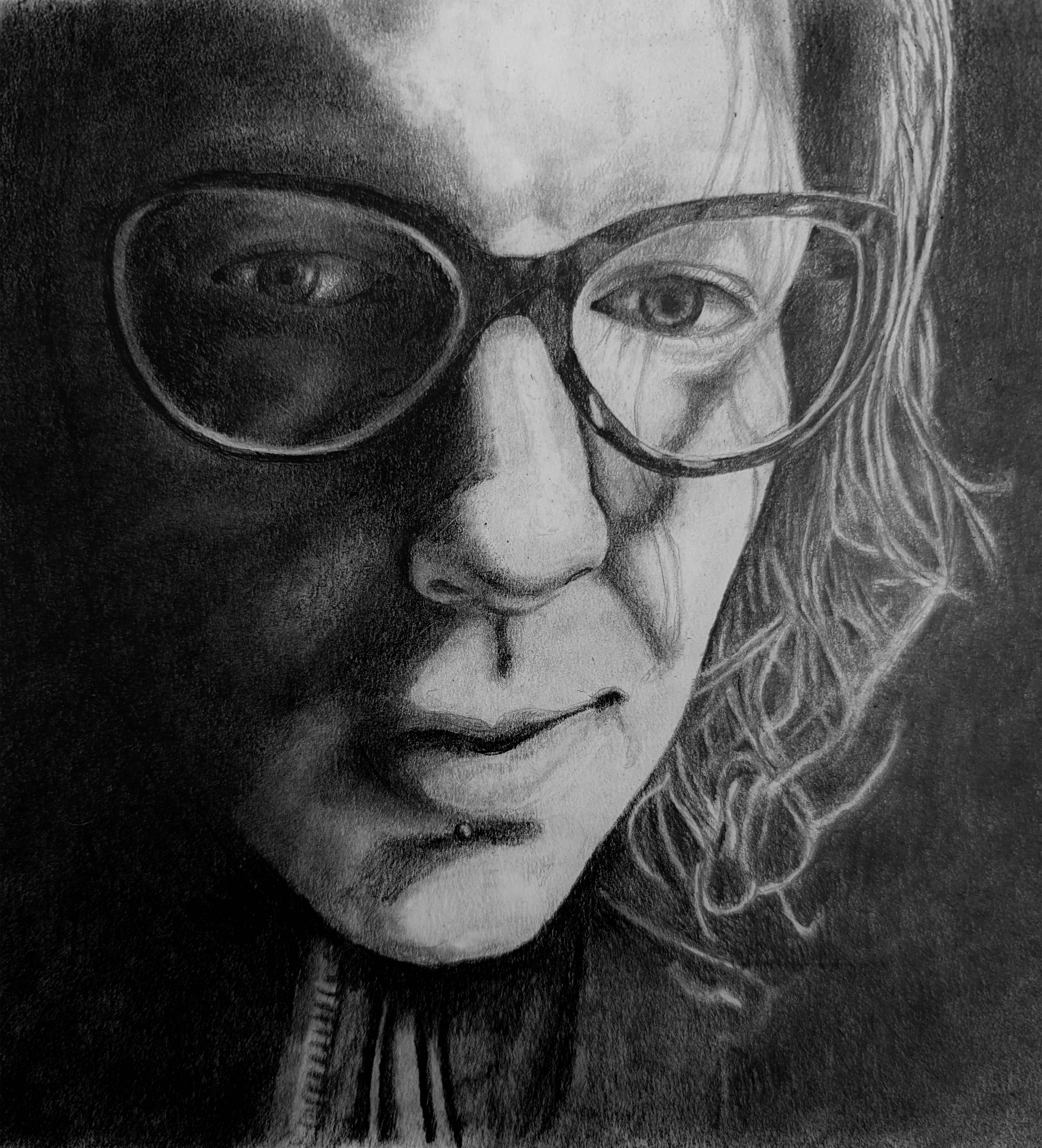 Image of a woman looking down. She has dark glasses and she is in a dark room. You can see her hair on the side of her face and a zipper on her sheet. She has a sad expression.