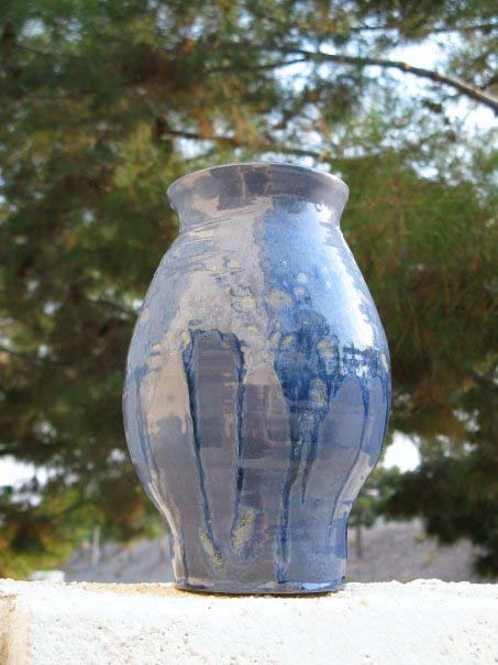 A vertical vase with a round middle section and tapered top and bottom. The glaze is light blue underneath with a darker blue glaze on the top that is dripping down the vase.